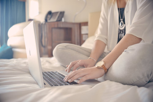 Kobieta siedzi na łóżku i korzysta z laptopa